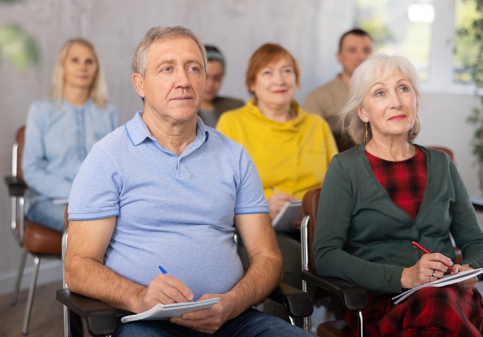 Positive interested elderly man listening attentively and taking notes on lesson during language courses for older adults